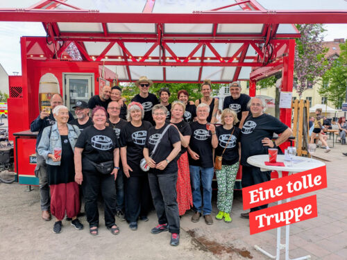 Gruppenbild mit 18 Personen vor dem Getränkewagen und Bildbeschriftung "Eine tolle Truppe"